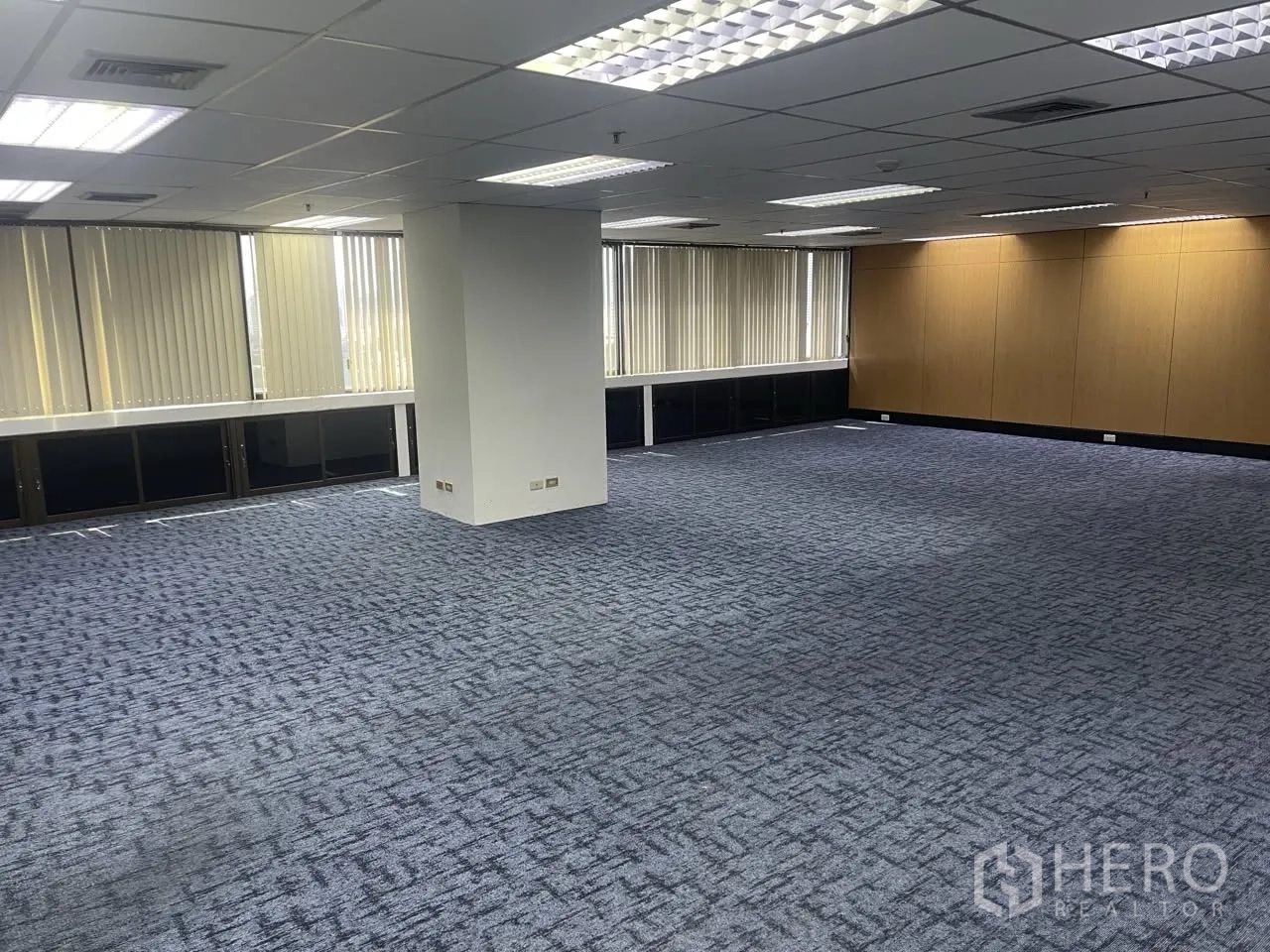 Office Space for rent in Khlong Toei, Bangkok - Open-plan office with a central pillar, wraparound windows, and suspended grid lighting.