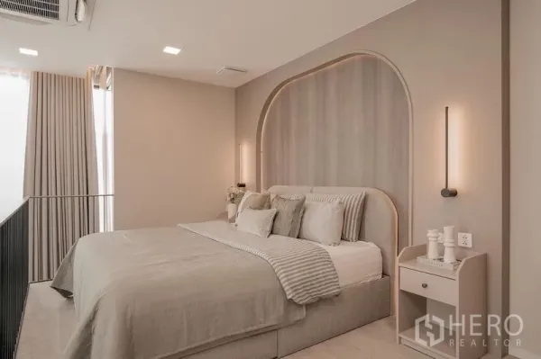 บ้าน ให้เช่า - ห้องนอนอบอุ่น มีหัวเตียงโค้ง ไฟติดผนัง โทนสีเอิร์ธ.