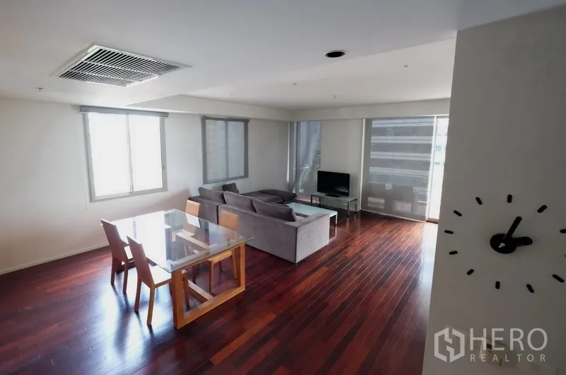 公寓 出租在Bang Rak, Bangkok - 客餐厅一体，深色木地板，玻璃餐桌、灰色沙发与落地窗旁电视。