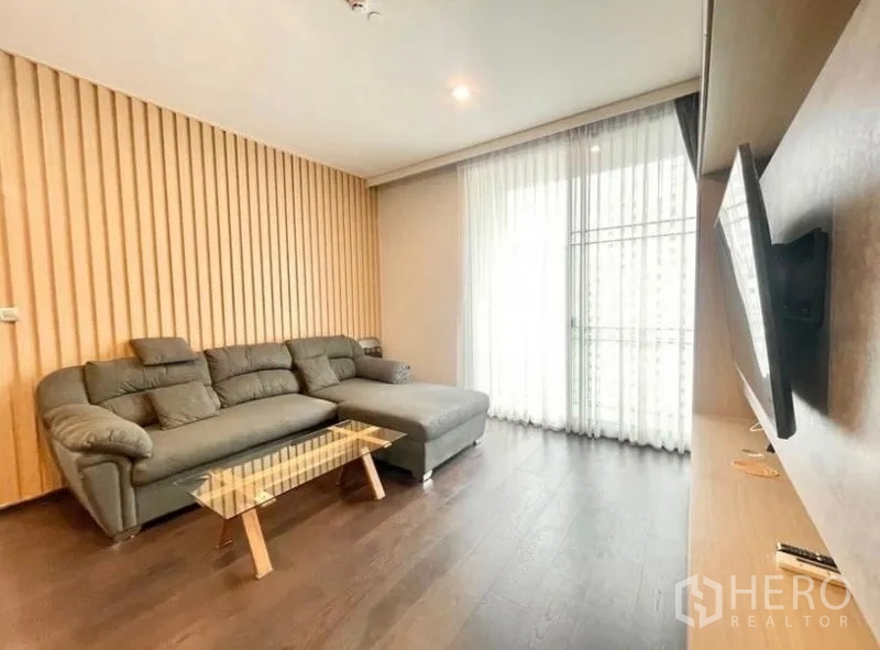 Condominium for rent in Watthana, Bangkok - Cozy lounge with L-shaped sofa, slatted wood feature wall and sheer curtains.