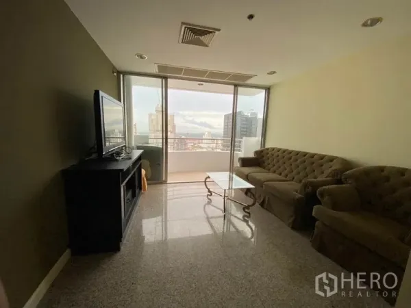 Condominium for rent in Watthana, Bangkok - Living room with sofa set and TV stand opening to a balcony with Bangkok skyline views through sliding glass doors.