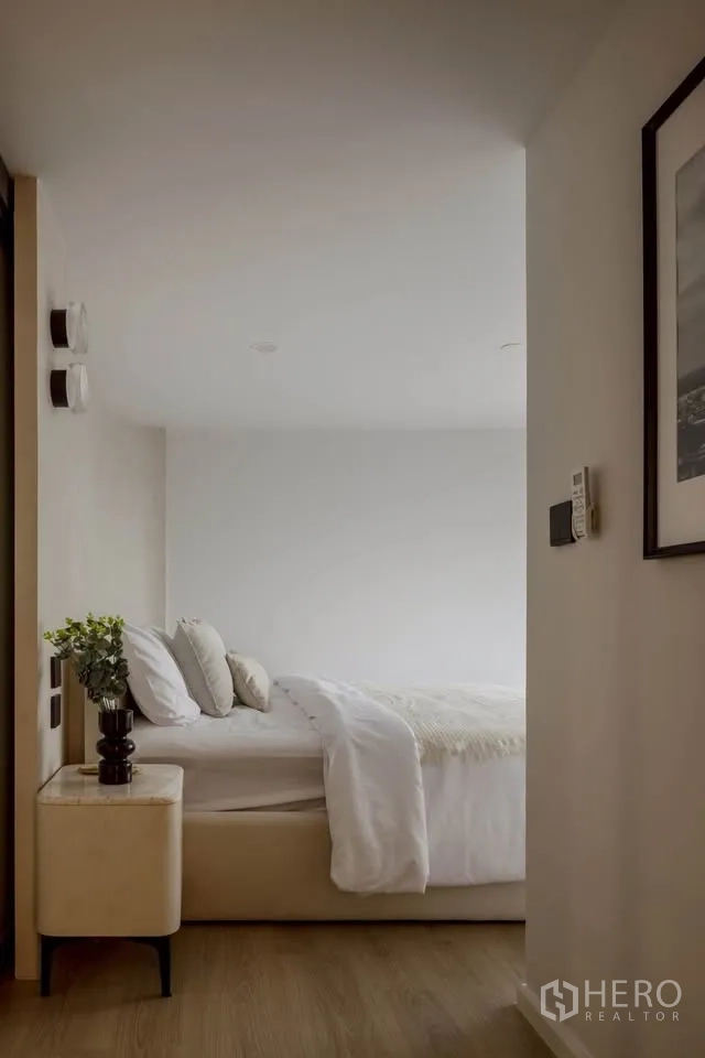 Condominium for rent in Khlong Toei, Bangkok - Cozy bedroom with upholstered bed, neutral bedding, bedside table with plant, and wood flooring.