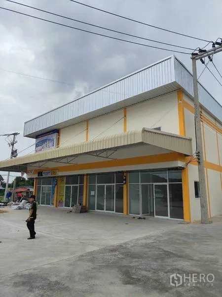 Warehouse for rent in Krathum Baen, Samut Sakhon - Corner warehouse unit with glass storefront and large canopy at the complex entrance.