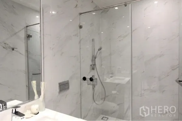 Condominium for rent in Bangkok - Glass-enclosed shower with handheld rain shower in a marble-clad bathroom.