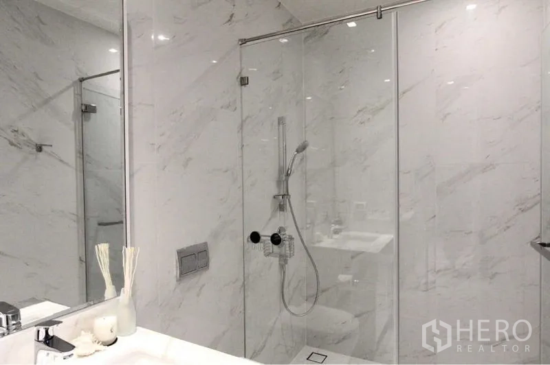 Condominium for rent in Bangkok - Glass-enclosed shower with handheld rain shower in a marble-clad bathroom.