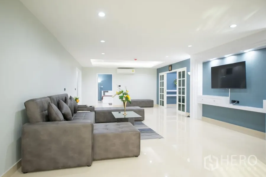 คอนโด ให้เช่าหรือขายในKhlong Toei, Bangkok - ห้องนั่งเล่นกว้างของคอนโดในกรุงเทพฯ พร้อมโซฟาหนังสีเทา ผนังทีวีบิลท์อิน ไฟดาวน์ไลท์ และประตูกระจก