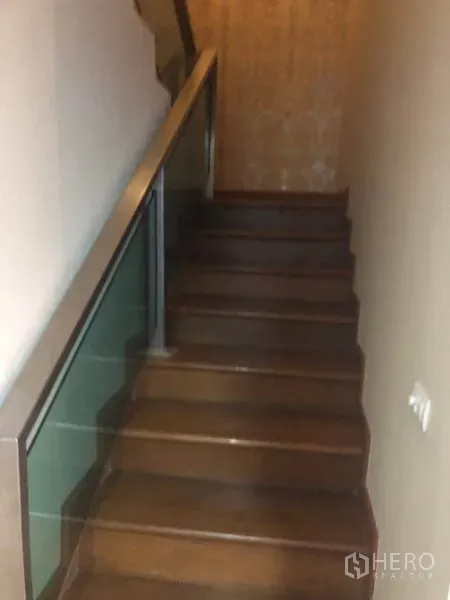 Condominium for sale in Bang Na, Bangkok - Wooden staircase with glass and metal railing leading up to the mezzanine level.