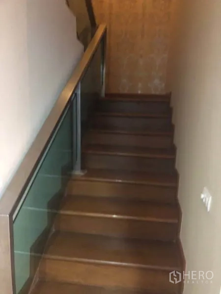 Condominium for sale in Bang Na, Bangkok - Wooden staircase with glass and metal railing leading up to the mezzanine level.