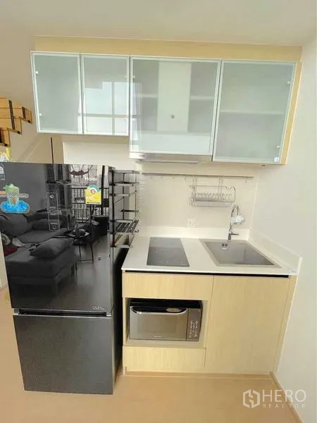 Condominium for rent in Watthana, Bangkok - Compact kitchenette with black fridge, induction cooktop, sink, and microwave.
