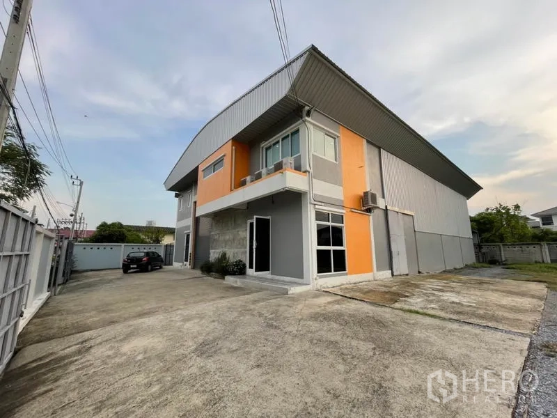 Warehouse for rent in Bang Kapi, Bangkok - Angled view of a two-storey warehouse with orange accents and a spacious front driveway.
