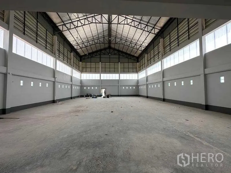 Factory for sale in Khlong Luang, Pathum Thani - Expansive high-ceiling warehouse hall with steel truss roof, clerestory windows and empty concrete floor.