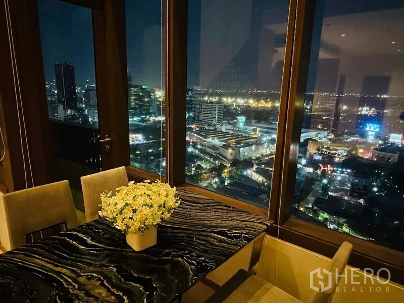 คอนโด ให้เช่าในBangkok - โต๊ะอาหารหินอ่อนพร้อมแจกันดอกไม้ และวิวเมืองยามค่ำผ่านกระจก