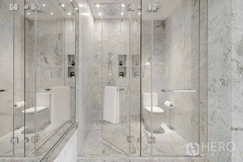 Condominium for sale in Watthana, Bangkok - Contemporary marble bathroom with glass partitions, shower and toilet.