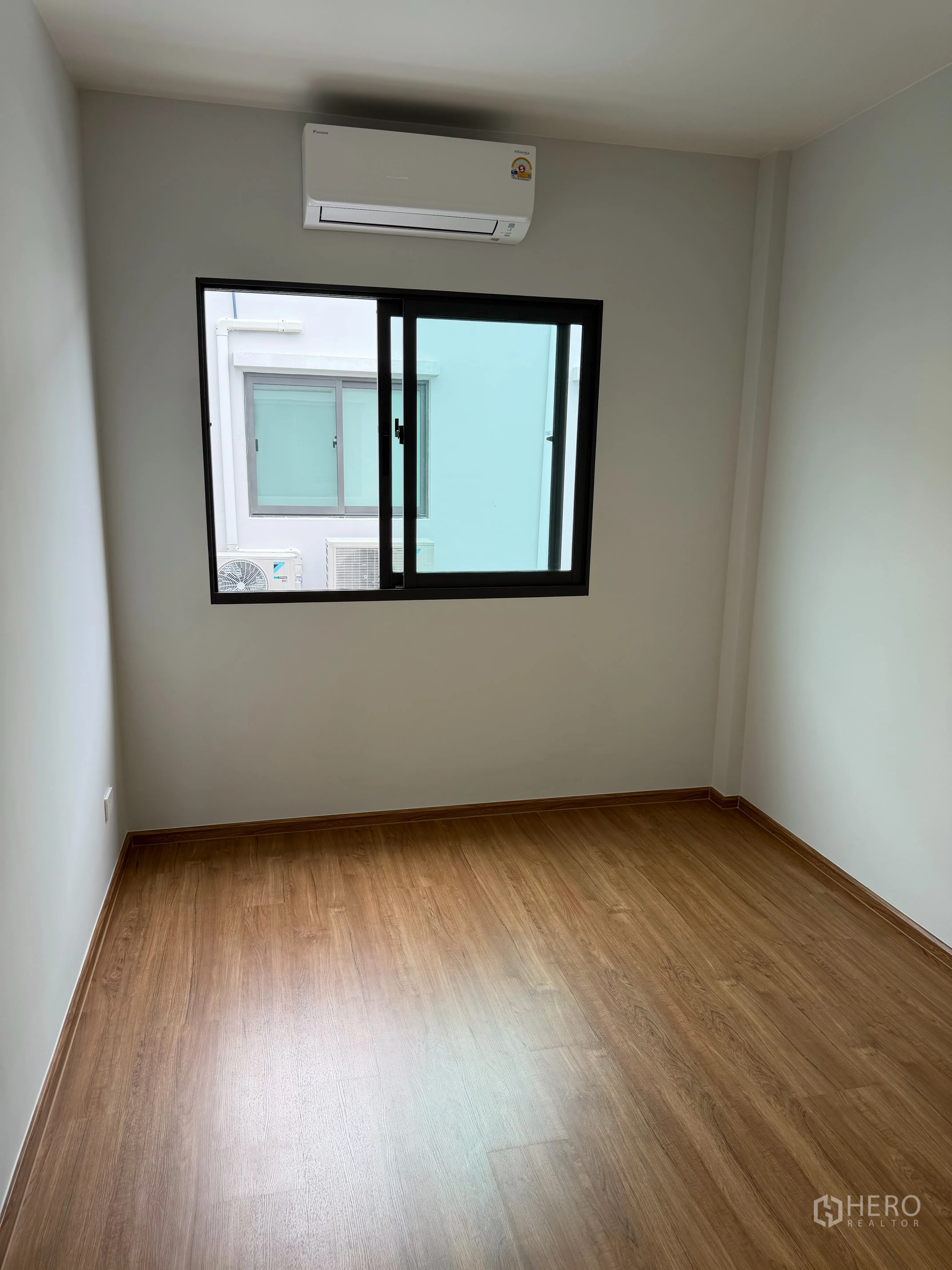 Townhouse for rent in Bang Phli, Samut Prakan - Bright bedroom with wood flooring, window, and wall-mounted air conditioner.