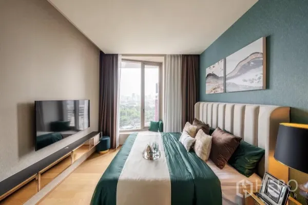 Condominium for rent in Bang Rak, Bangkok - Bright bedroom with upholstered headboard, wall-mounted TV and floor-to-ceiling window overlooking the city and park.