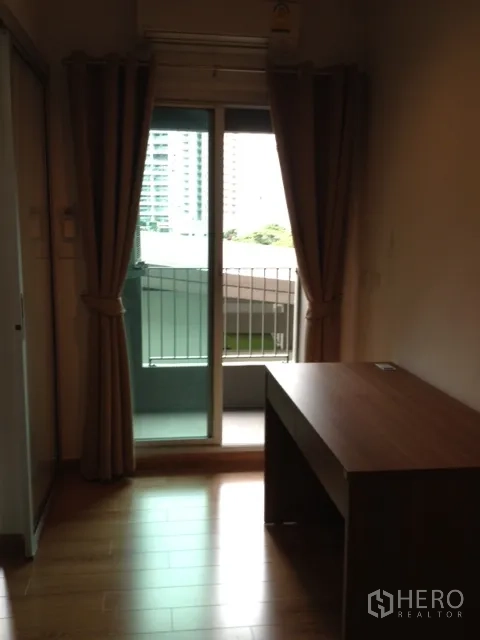 คอนโด ให้เช่าในKhlong Toei, Bangkok - ประตูกระจกออกสู่ระเบียงขนาดเล็ก วิวเมือง พร้อมม่านสีน้ำตาลและโต๊ะทำงาน