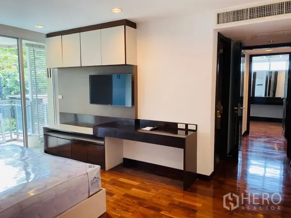 Condominium for rent in Watthana, Bangkok - Bedroom with built-in desk and TV unit beside floor-to-ceiling glass doors leading to the balcony.