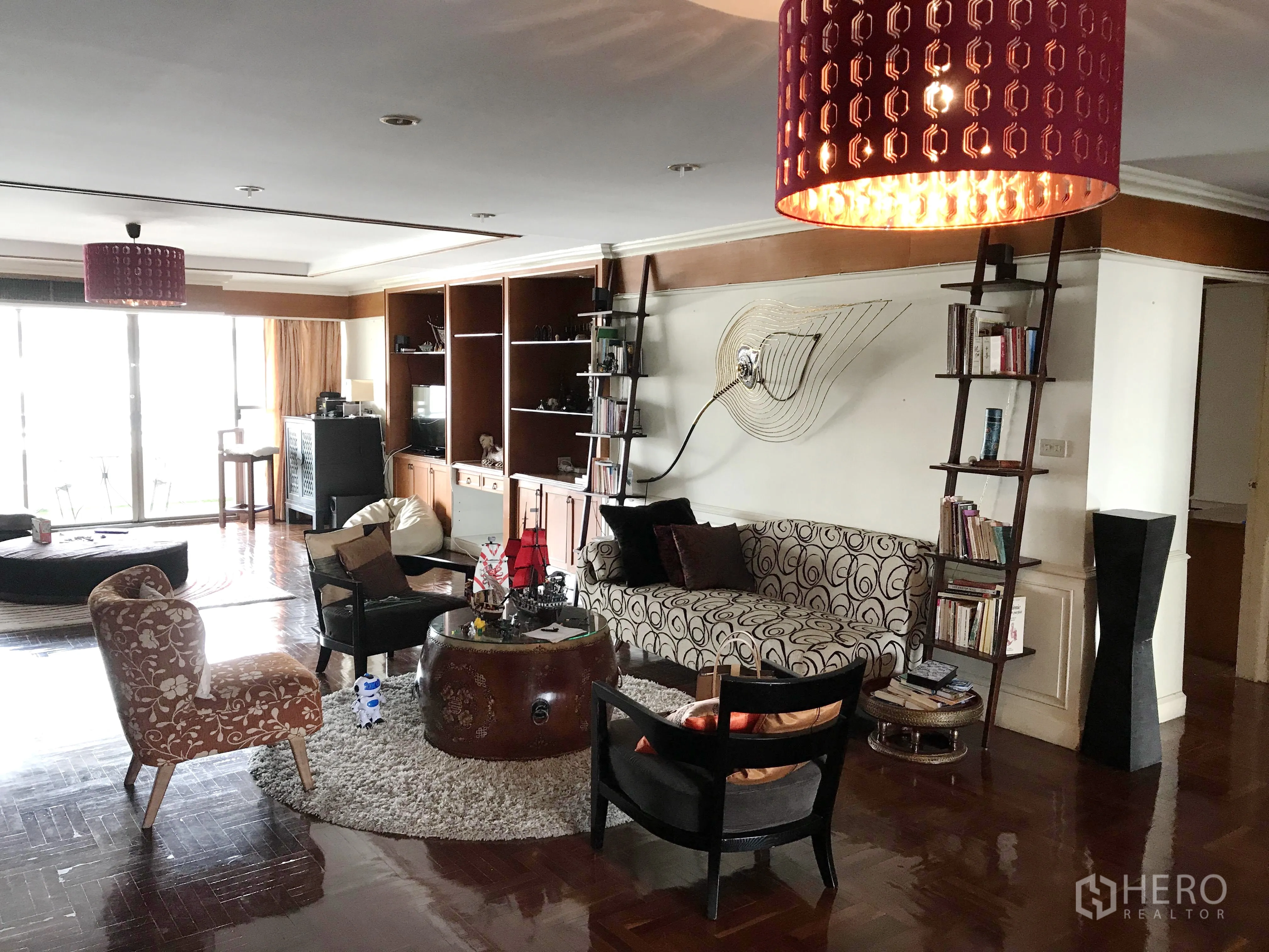 Condominium for rent in Watthana, Bangkok - Spacious living room with polished hardwood floors, built-in shelves, feature wall art and sliding glass doors opening to a bright balcony.