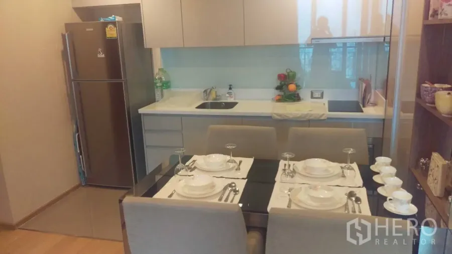 Condominium for rent in Ratchathewi, Bangkok - Modern kitchenette with white cabinets, stainless refrigerator and a dining table set for four.