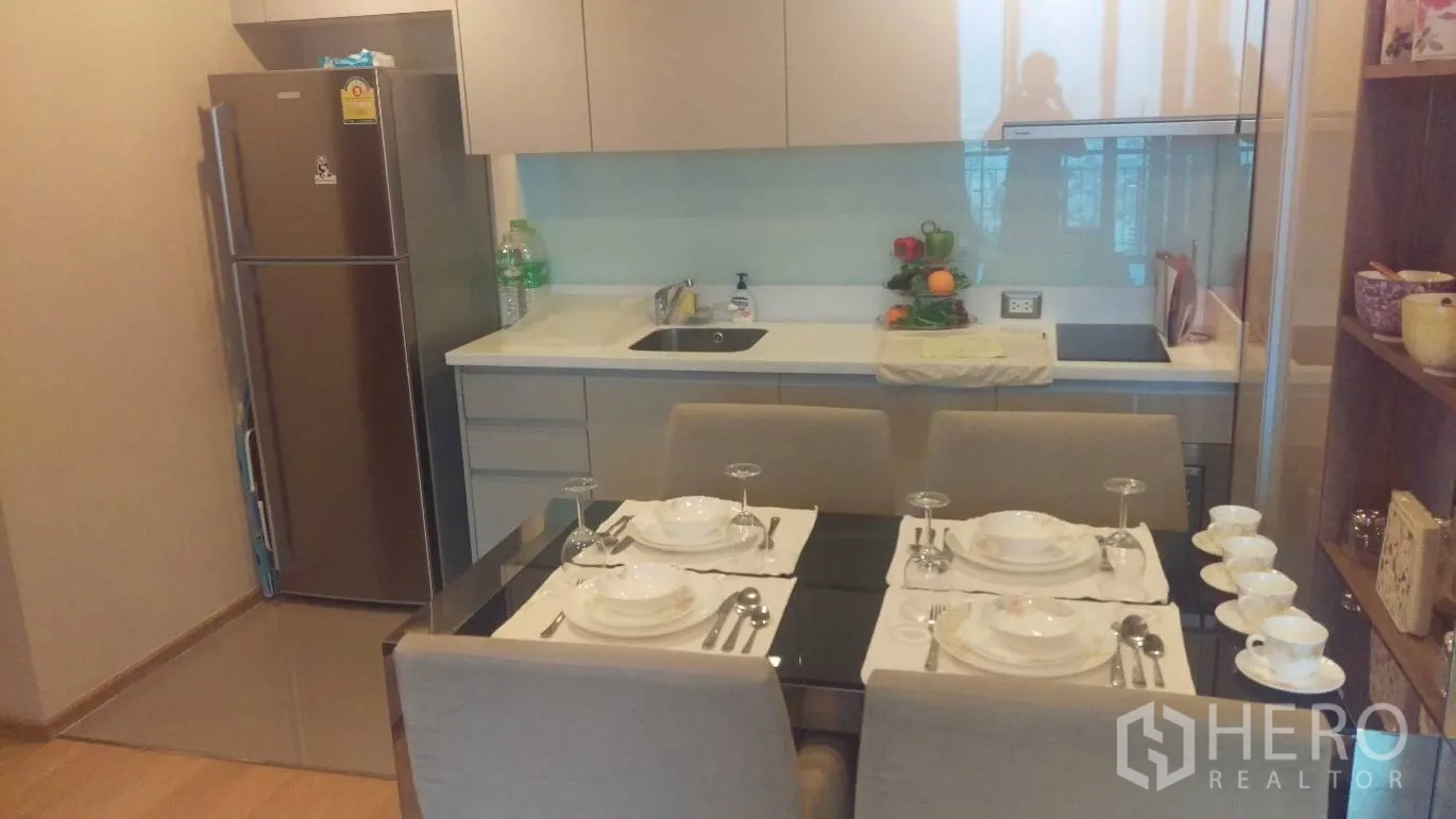 Condominium for rent in Ratchathewi, Bangkok - Modern kitchenette with white cabinets, stainless refrigerator and a dining table set for four.