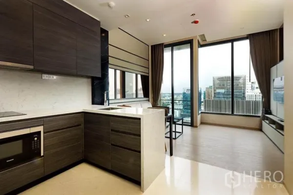 Condominium for rent or sale in Watthana, Bangkok - L-shaped kitchen and bright living room with expansive windows over Bangkok.
