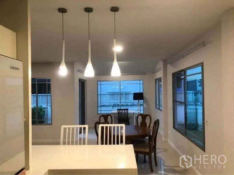 Detached House for rent in Prawet, Bangkok - Kitchen island with white stools facing the dining area and wide windows.