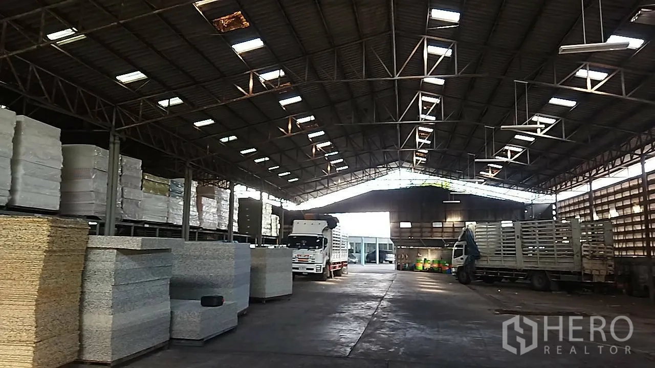 Warehouse for rent in Bang Khun Thian, Bangkok - Central loading area inside the warehouse with trucks, concrete floor, and roof lights.