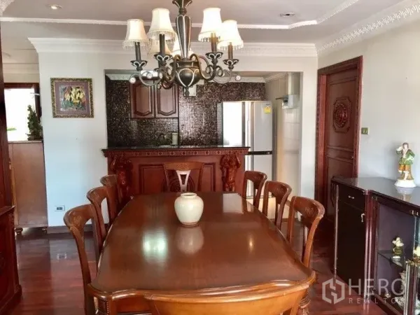 Condominium for rent or sale in Pathum Wan, Bangkok - Dining room with chandelier facing a carved breakfast bar and kitchen pass-through.