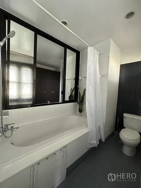 公寓 出租在Khlong Toei, Bangkok - 浴室配浸泡浴缸、淋浴与马桶，旁有窗户。