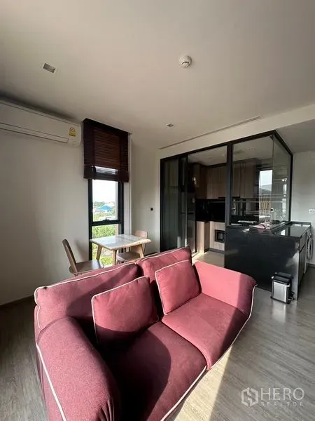 Condominium for rent in Watthana, Bangkok - Sunlit living area at Mori Haus with maroon sofa, dining table, and glass kitchen partition.