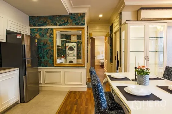 Condominium for rent in Watthana, Bangkok - Open-plan kitchen and dining with white cabinets, mosaic backsplash, stainless fridge, and an in-unit washer–dryer reflected in a gold-framed mirror.