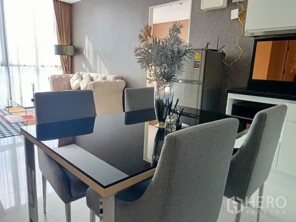 คอนโด ให้เช่าในWatthana, Bangkok - พื้นที่รับประทานอาหารแบบโอเพ่นแปลน โต๊ะกระจกสีดำ เก้าอี้ผ้าเทา ครัวขนาดกะทัดรัดและตู้เย็น เชื่อมต่อสู่ห้องนั่งเล่นที่มีหน้าต่างสูงโปร่ง.