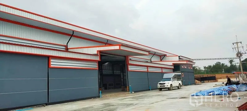 โรงงาน ให้เช่าหรือขายในPhanat Nikhom, Chon Buri - ด้านหน้าอาคารยาว มีประตูขนถ่ายหลายจุดและรถกระบะจอดที่ลาน