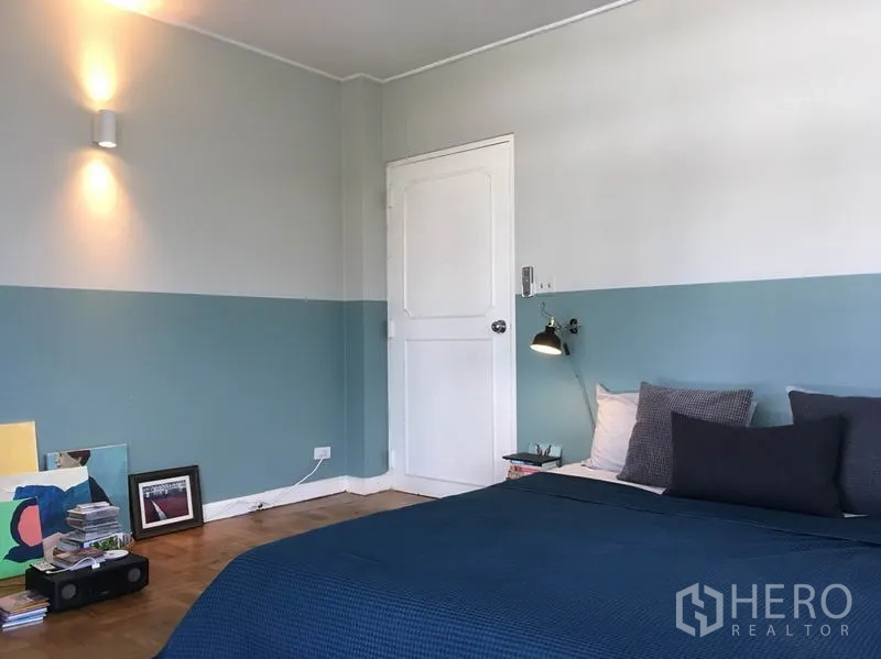 Apartment for rent in Khlong Toei, Bangkok - Spacious bedroom corner with wall lights, white door, parquet floor, and simple decor.