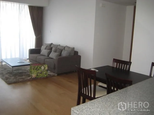 Condominium for rent or sale in Sathon, Bangkok - Bright lounge with gray sofa, coffee table, dining set and full-height curtains in a Bangkok condominium.
