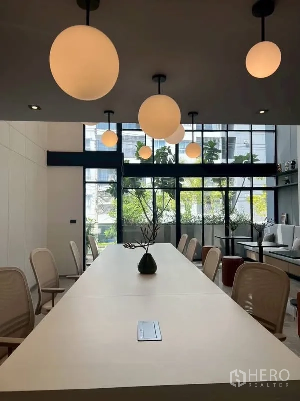 Home Office for rent or sale in Mueang Samut Prakan, Samut Prakan - Long conference table beneath spherical lights overlooking greenery through a glass wall.