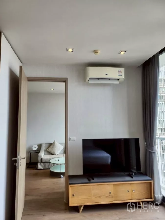 Condominium for rent in Khlong Toei, Bangkok - TV console and wall AC facing the living area with sofa and round glass coffee table.