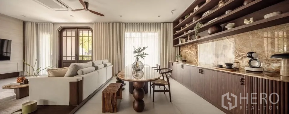 Detached House for rent or sale in Lat Krabang, Bangkok - Open-plan living and dining with white sectional sofa, stone feature wall, and long shelves.