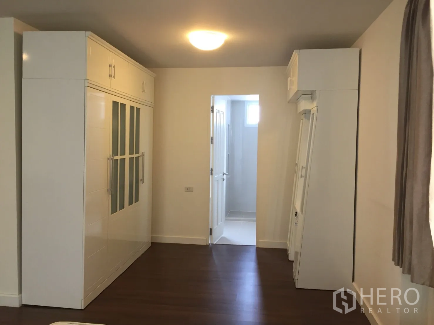 联排别墅 出租在Watthana, Bangkok - 卧室走道配内置白色衣柜，木地板，通往套内卫浴的门。