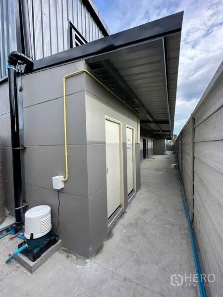 Warehouse for rent in Bang Bua Thong, Nonthaburi - Exterior utility area showing restroom block, piping, and a covered walkway along the warehouse side.