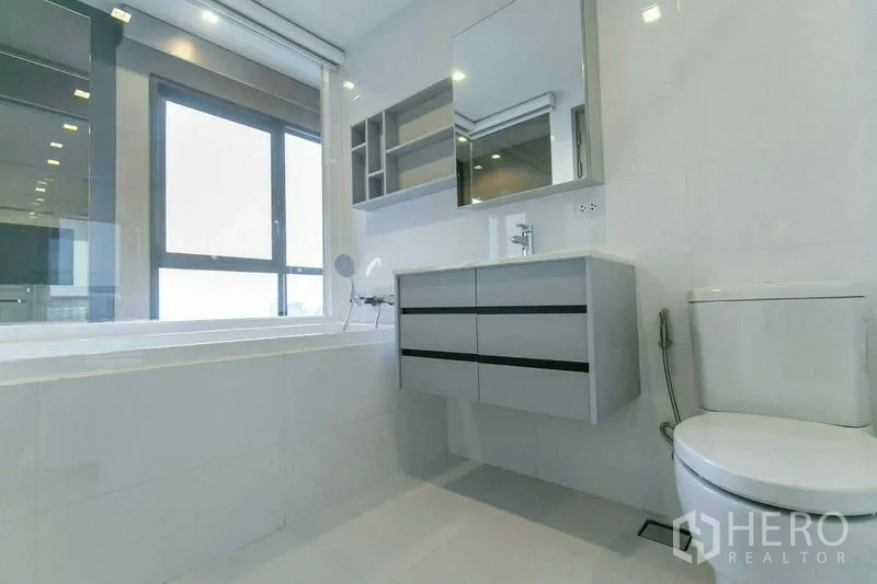 Condominium for rent or sale in Watthana, Bangkok - Bathroom with soaking tub beside a large window, floating vanity and mirrored storage.
