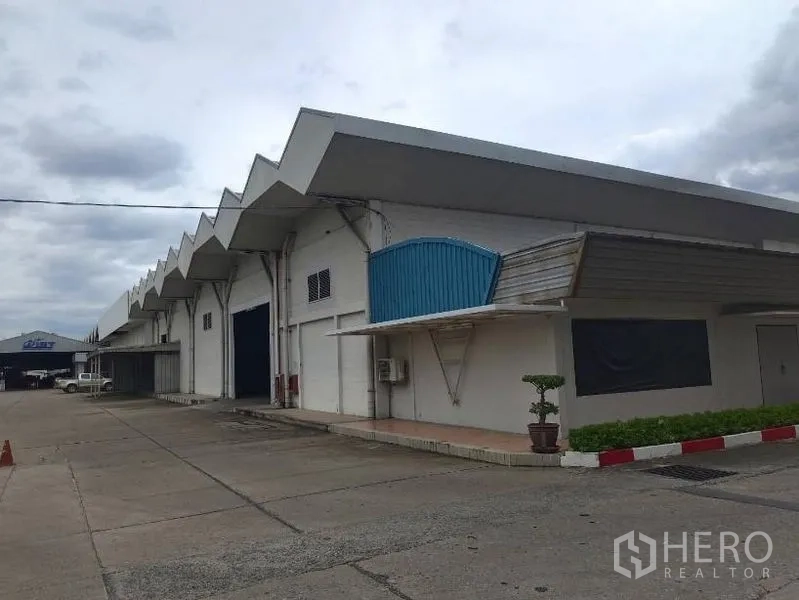货栈 出租在Lam Luk Ka, Pathum Thani - 锯齿形屋顶的大型仓库外观，设多处装卸门与宽阔混凝土车道。