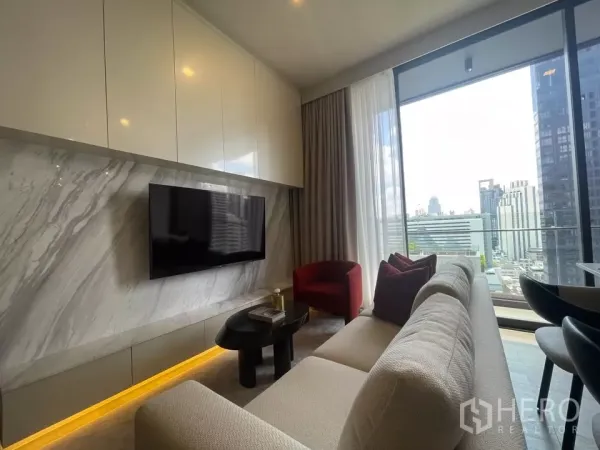 Condominium for rent in Watthana, Bangkok - Living area with marble TV wall, red accent chair and balcony showcasing skyline views.