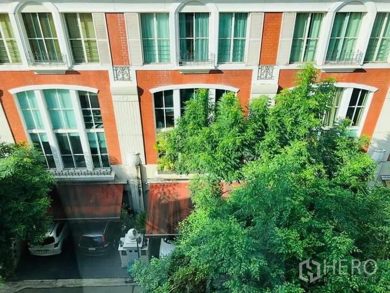 Townhouse for rent in Khlong Toei, Bangkok - Red-brick townhouse facade with tall arched windows, mature trees and covered parking bays.