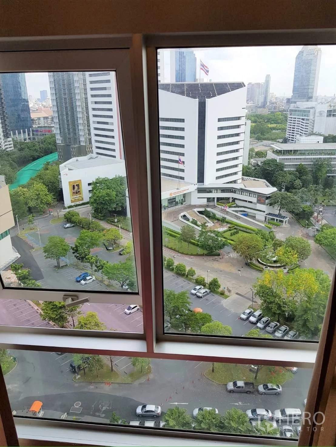 Condominium for rent in Huai Khwang, Bangkok - Window view overlooking modern office buildings, greenery, and a parking area below.
