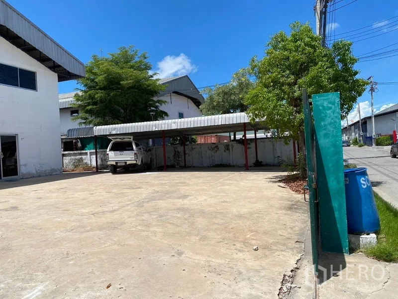 Factory for rent or sale in Bang Phli, Samut Prakan - Concrete forecourt with covered parking bays and shade trees beside the factory.