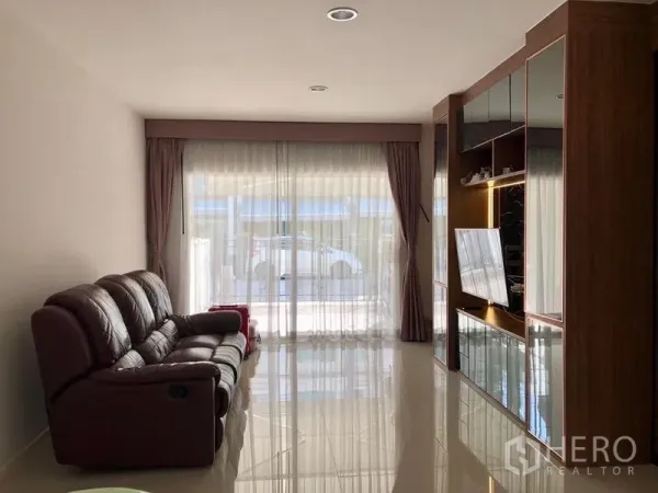 联排别墅 出租在Suan Luang, Bangkok - 明亮客厅，深色皮沙发、亮面地砖与整面高帘。