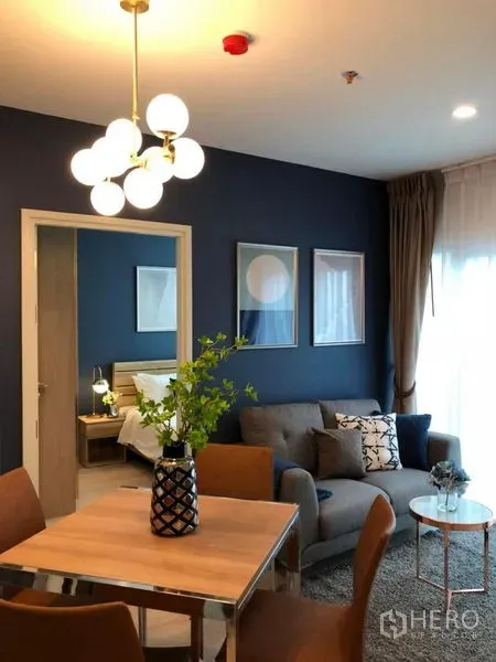 คอนโด ขาย - ห้องนั่งเล่นมีโซฟาและชุดทานอาหาร ผนังสีน้ำเงิน โคมไฟทรงกลม และประตูเชื่อมห้องนอน