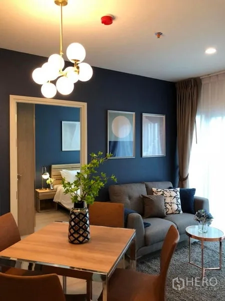 คอนโด ขาย - ห้องนั่งเล่นมีโซฟาและชุดทานอาหาร ผนังสีน้ำเงิน โคมไฟทรงกลม และประตูเชื่อมห้องนอน