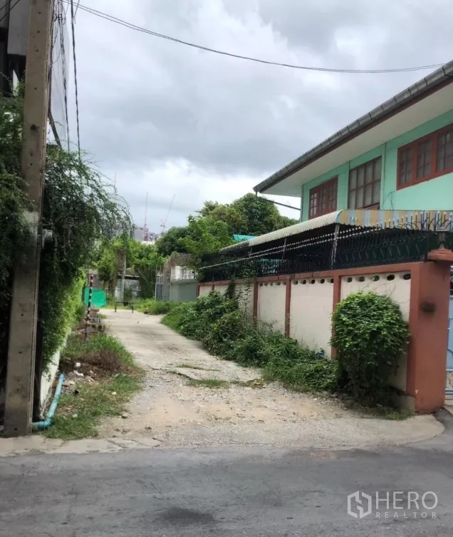 ที่ดิน ขายในPhra Khanong, Bangkok - ซอยที่อยู่อาศัยแคบมีต้นไม้และกำแพงรั้ว นำทางเข้าสู่ทางเข้าที่ดินที่มีประตู.